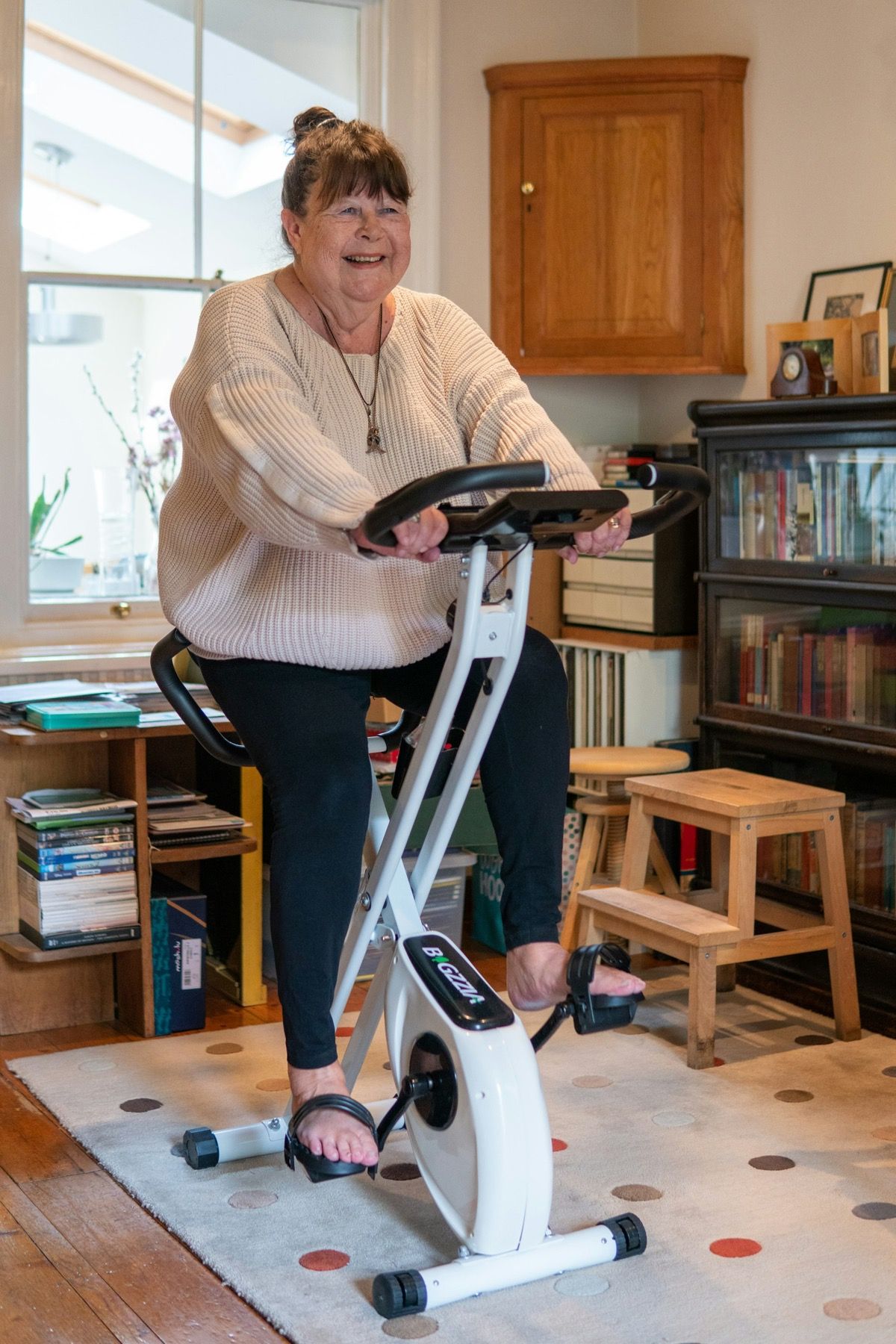 Une femme pédale sur un vélo d’appartement installé dans son salon.