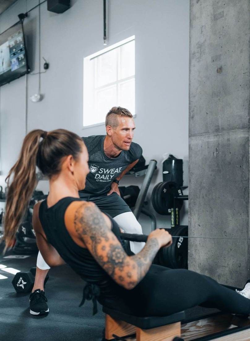 Un coach accompagne une cliente pendant un exercice de tirage, en salle de sport.